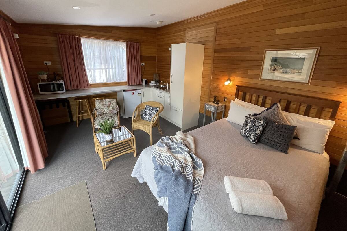 A cozy room with a bed, a desk, a small kitchenette, and a window with curtains.