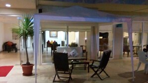 An outdoor seating area with a covered table and chairs, a potted plant, and a red carpet. - Mikado Hotel (Alanya)