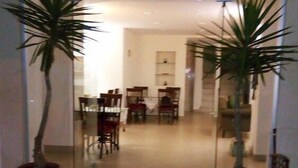 A modern interior with a red carpet leading to a dining area with chairs and a table. There are two potted plants on either side of the entrance. - Mikado Hotel (Alanya)