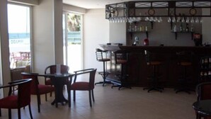 A bar area with multiple stools and a counter, a seating area with tables and chairs, and a view of the outdoors through large windows. - Mikado Hotel (Alanya)
