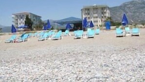 A beach with sun loungers and umbrellas, a building with a balcony, and a mountainous backdrop. - Mikado Hotel (Alanya)