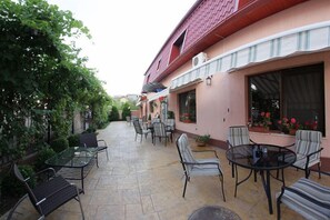 A patio area with outdoor seating and a building with a red roof and pink walls. - Vila Toparceanu (Otopeni)
