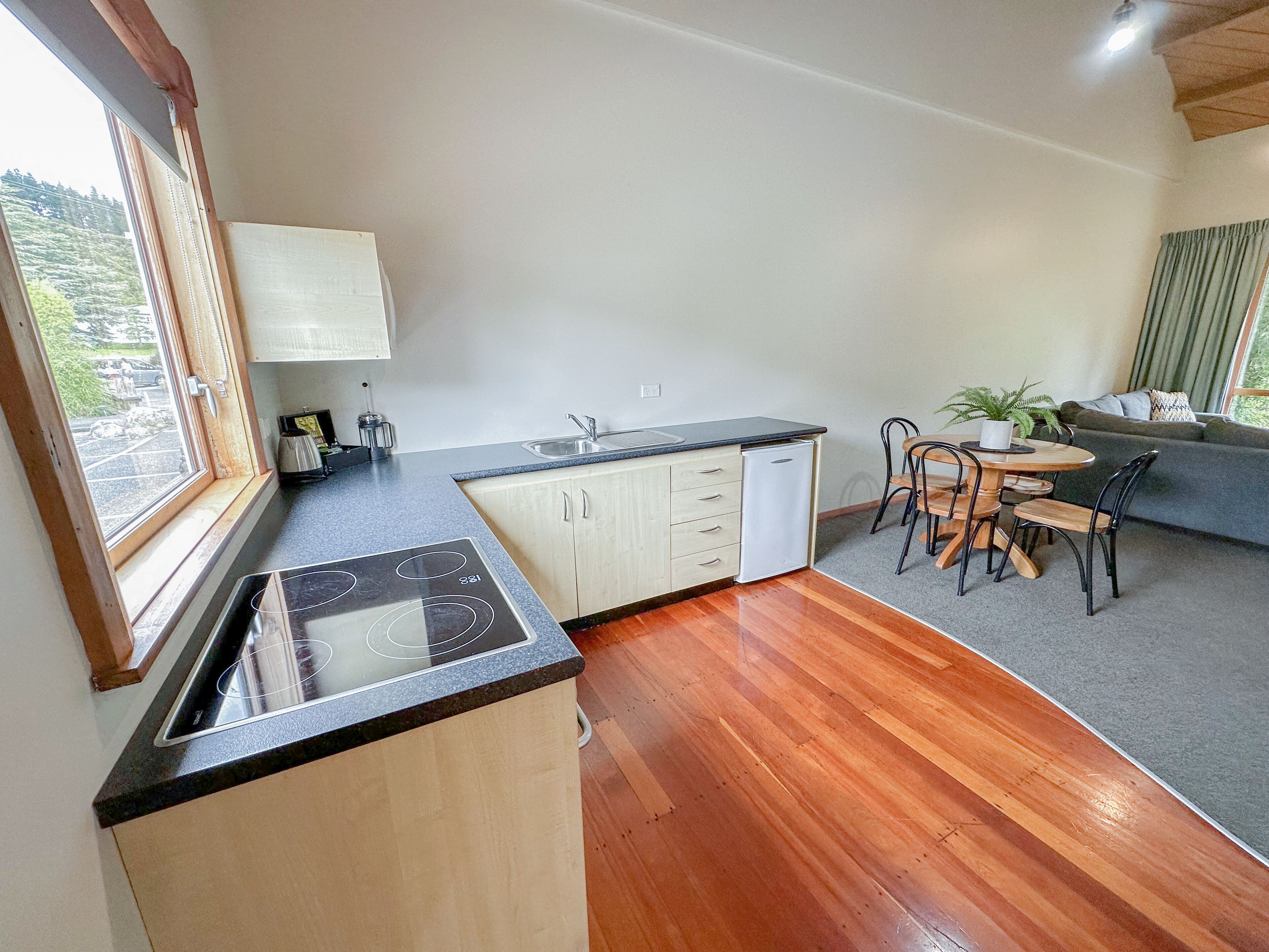 A compact kitchen with a built-in stove, a sink, and a dishwasher. There's a dining area with a round table and chairs, and a sofa in the living space.
