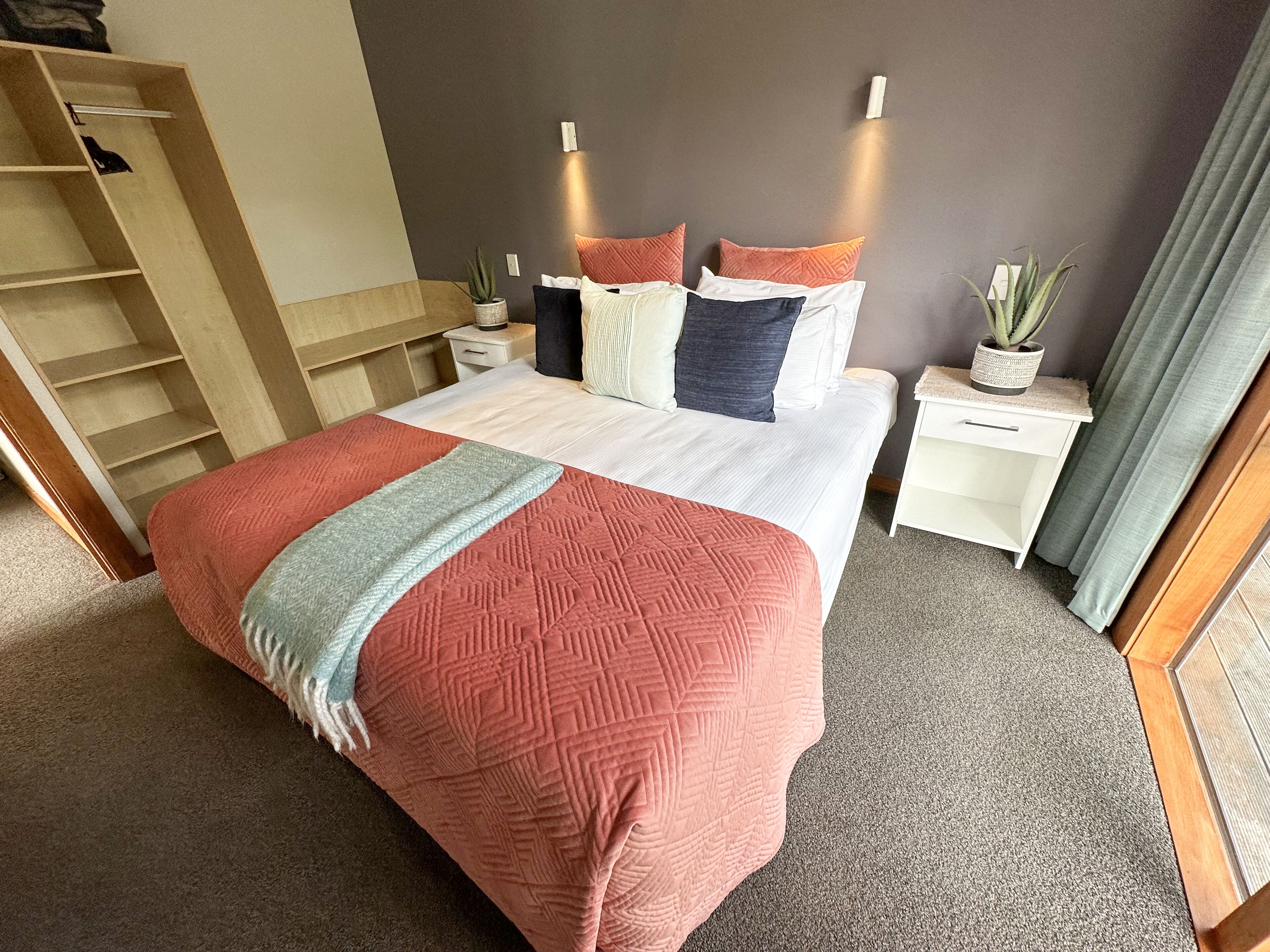 A neatly arranged bedroom with a bed, bedside tables, a wardrobe, and a potted plant.