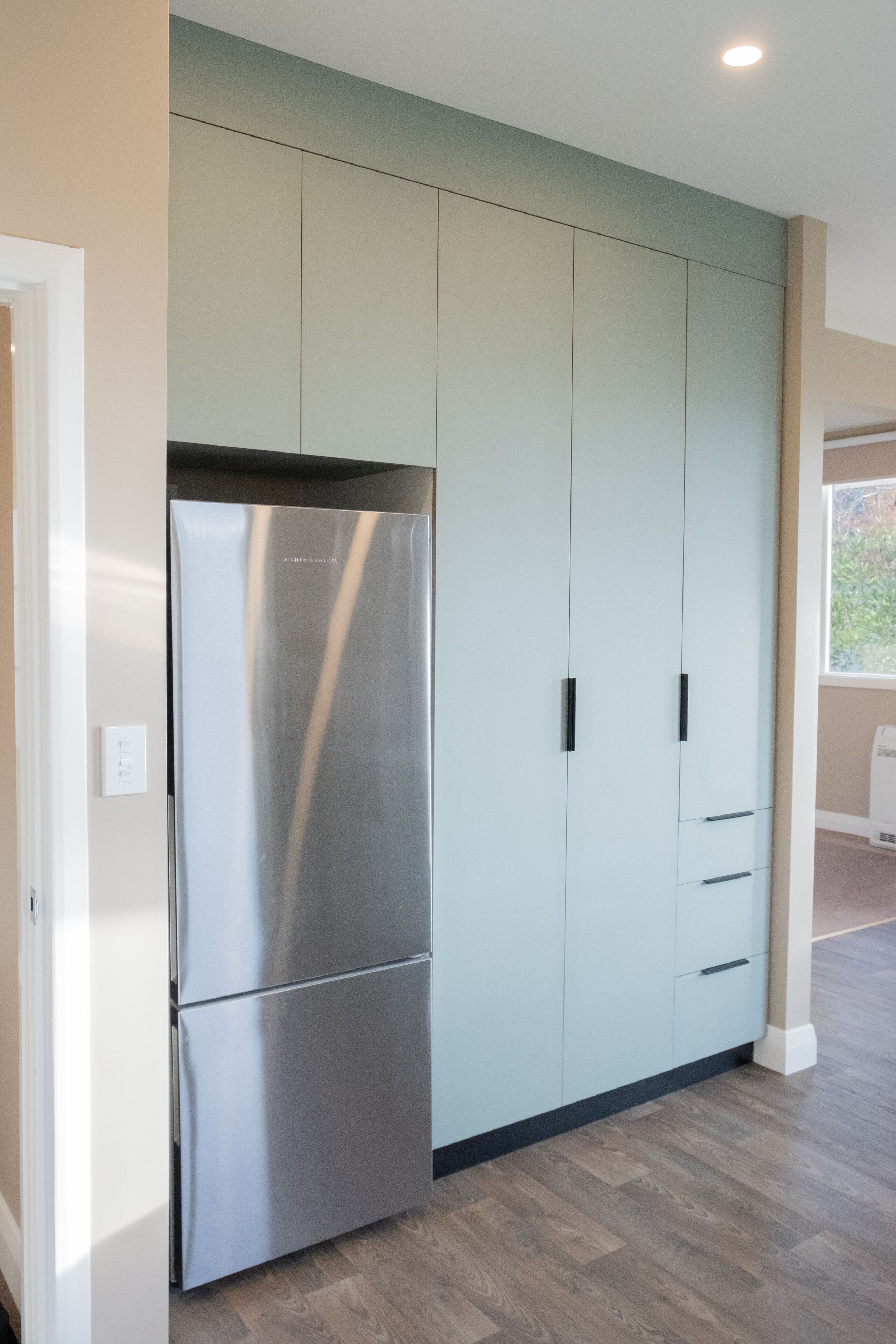 Une cuisine moderne avec un réfrigérateur en acier inoxydable, des meubles de couleur claire et un plancher en bois.