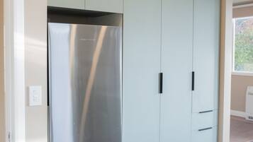 A modern kitchen with a stainless steel refrigerator, light-colored cabinets, and a wooden floor.