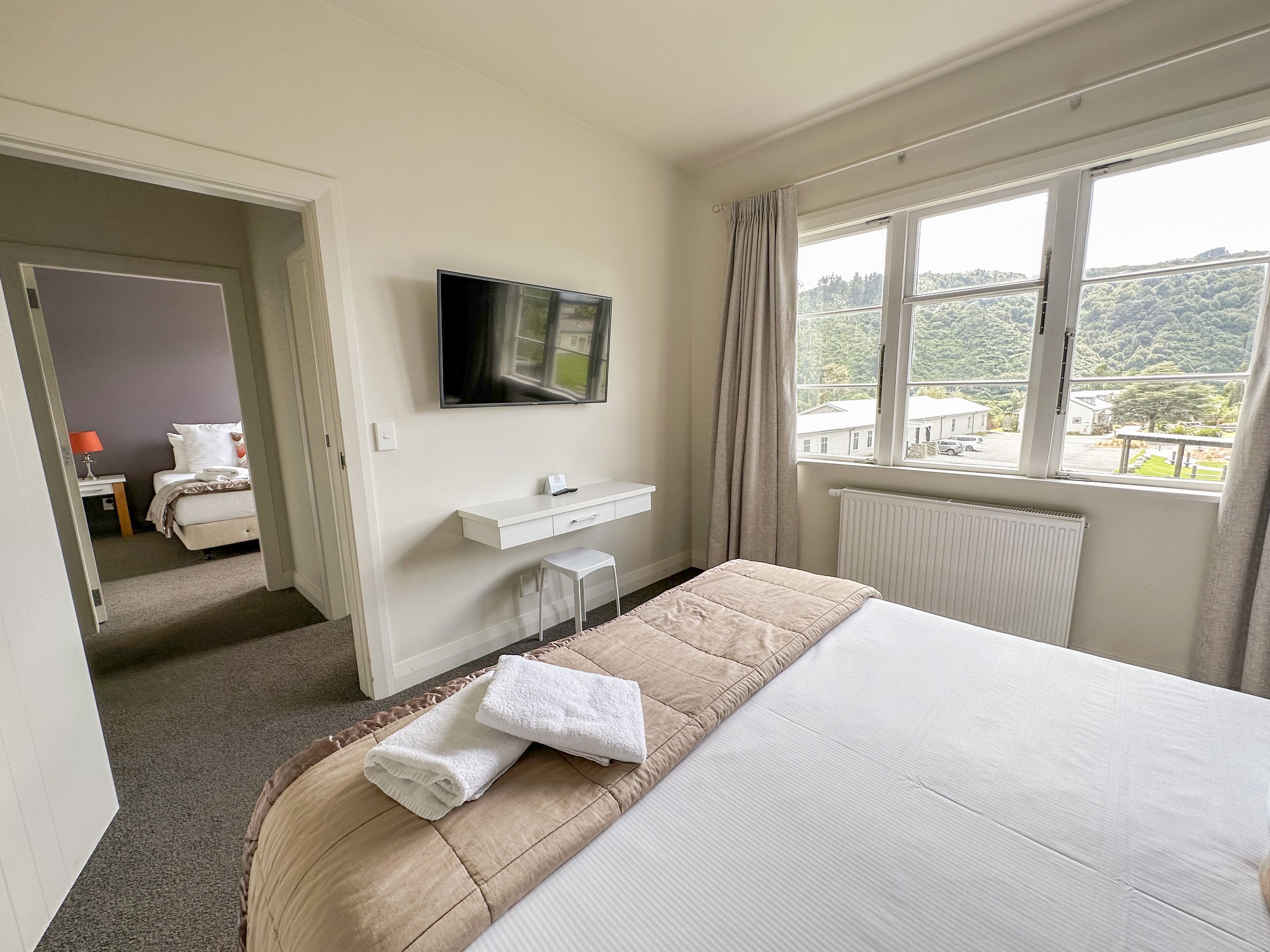 Een hotelkamer met een bed, een tv aan de muur, een bureau met stoel, en een raam met uitzicht op de omgeving.