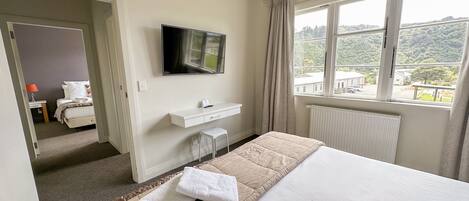 Een hotelkamer met een bed, een tv aan de muur, een bureau met stoel, en een raam met uitzicht op de omgeving.