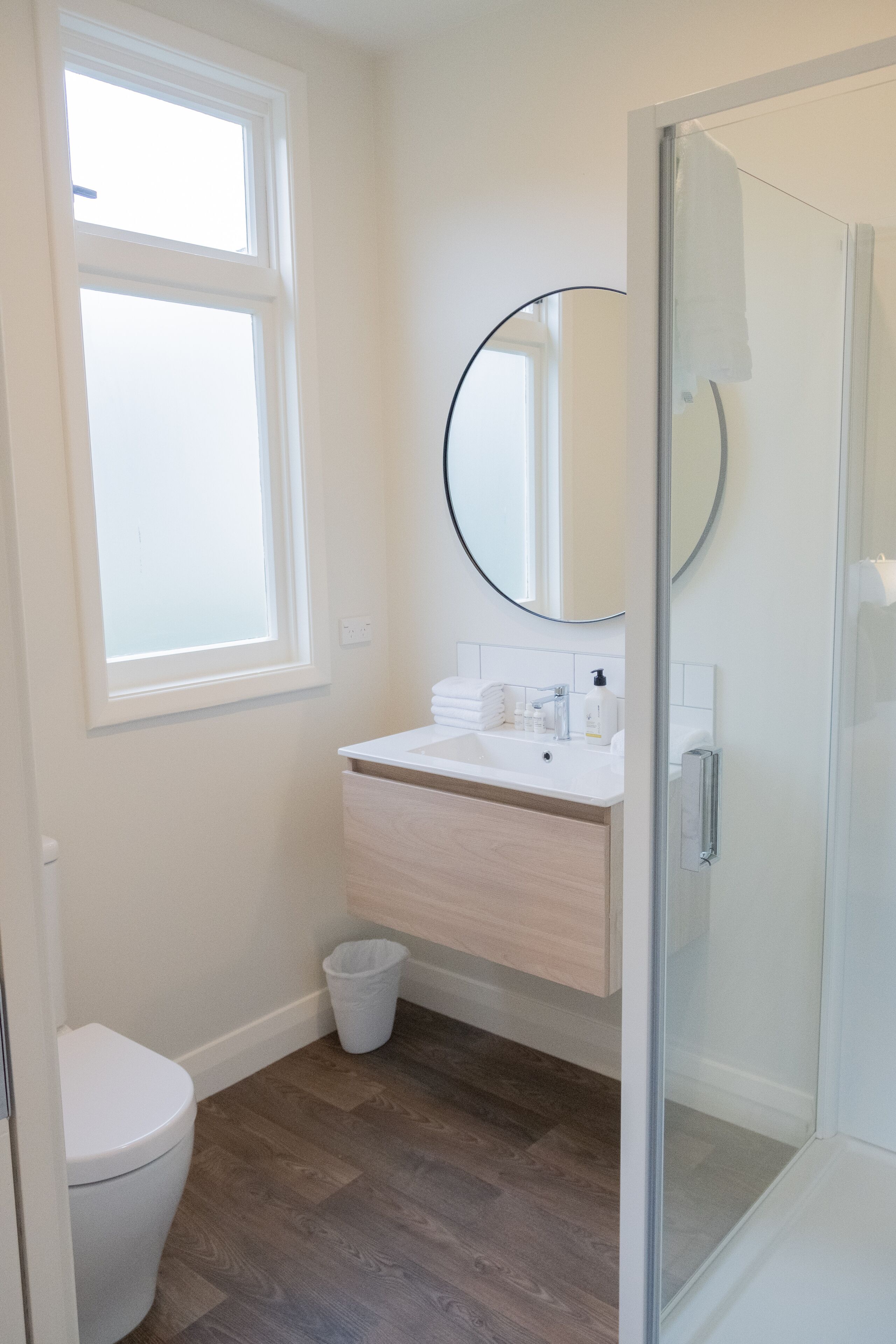 A bathroom with a toilet, a sink with a mirror, a glass shower enclosure, and a window.