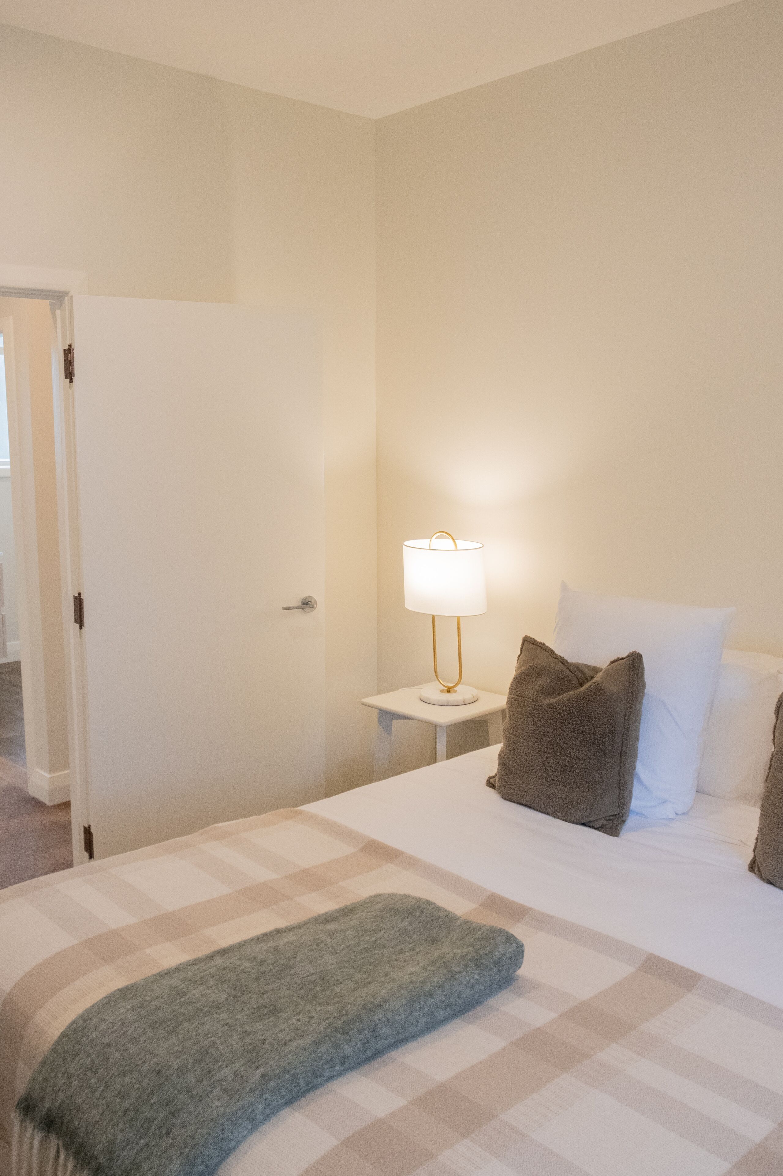 A hotel room with a bed, a bedside lamp, and a door.