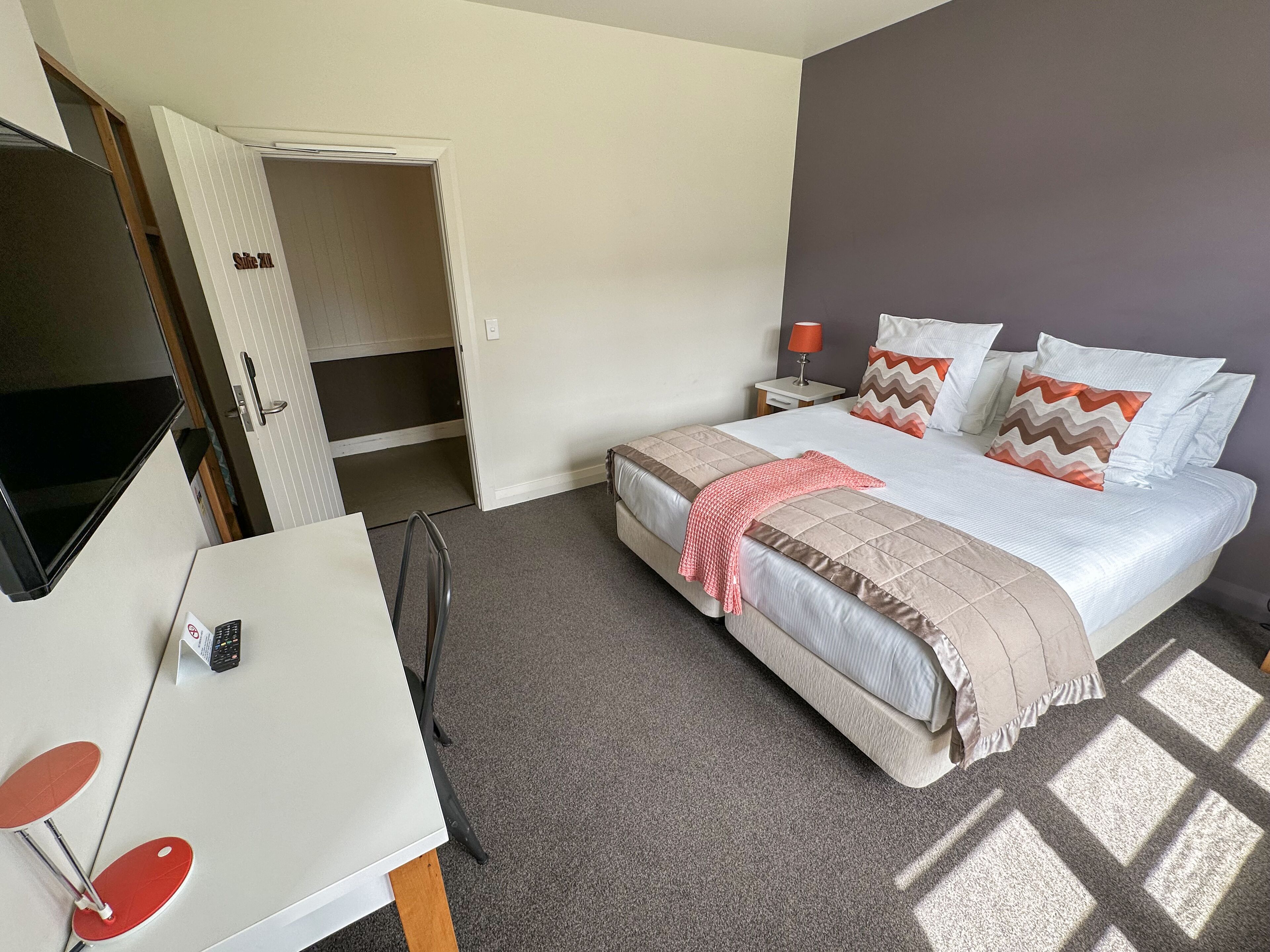 A hotel room with a bed, a desk, a TV, and a door leading to a bathroom.