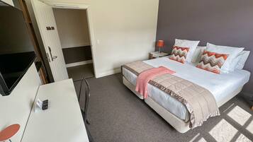 A hotel room with a bed, a desk, a TV, and a door leading to a bathroom.