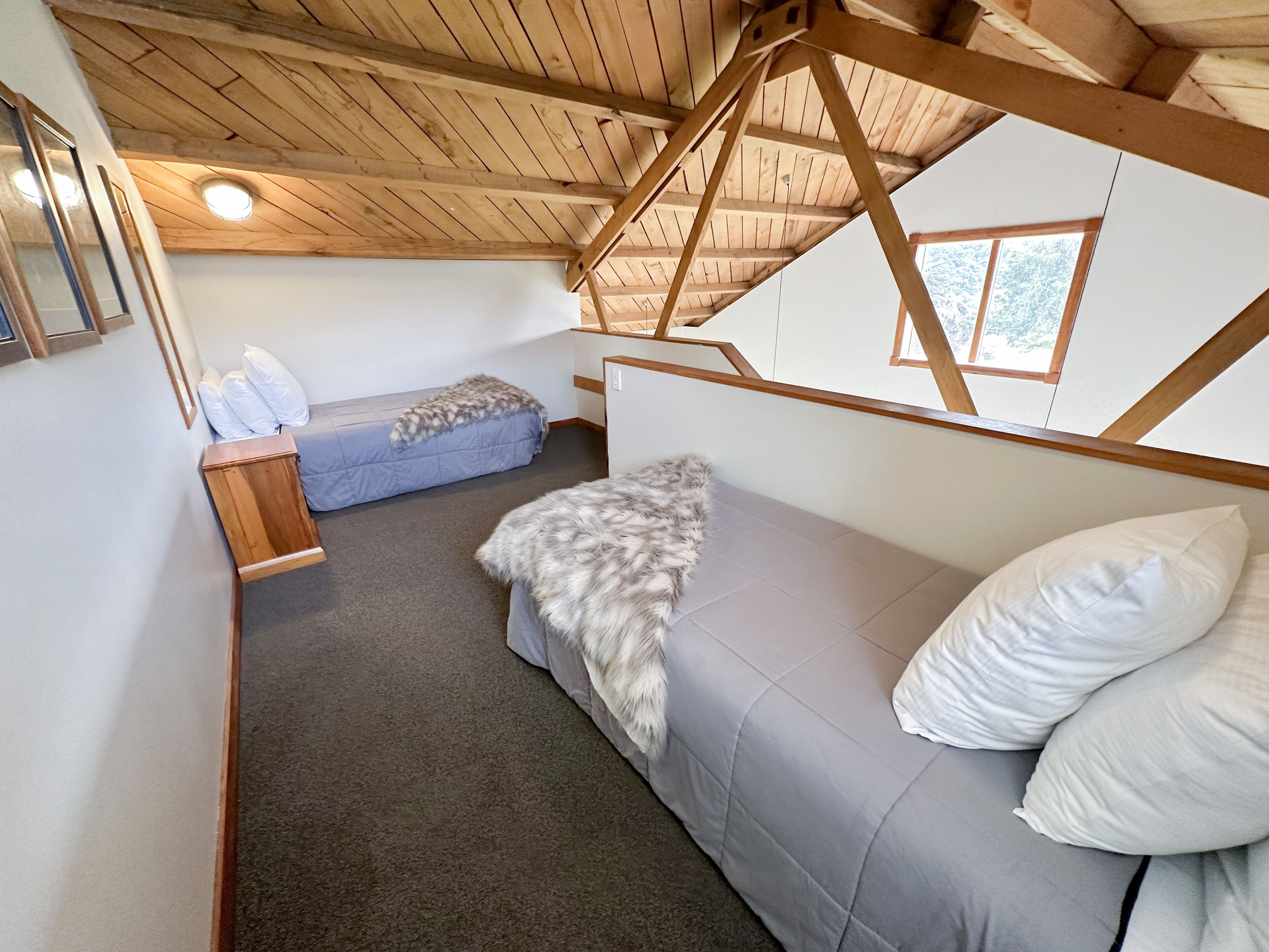 A cozy bedroom with a loft-style ceiling, a grey sofa, a fluffy throw blanket, and a bed with white pillows.