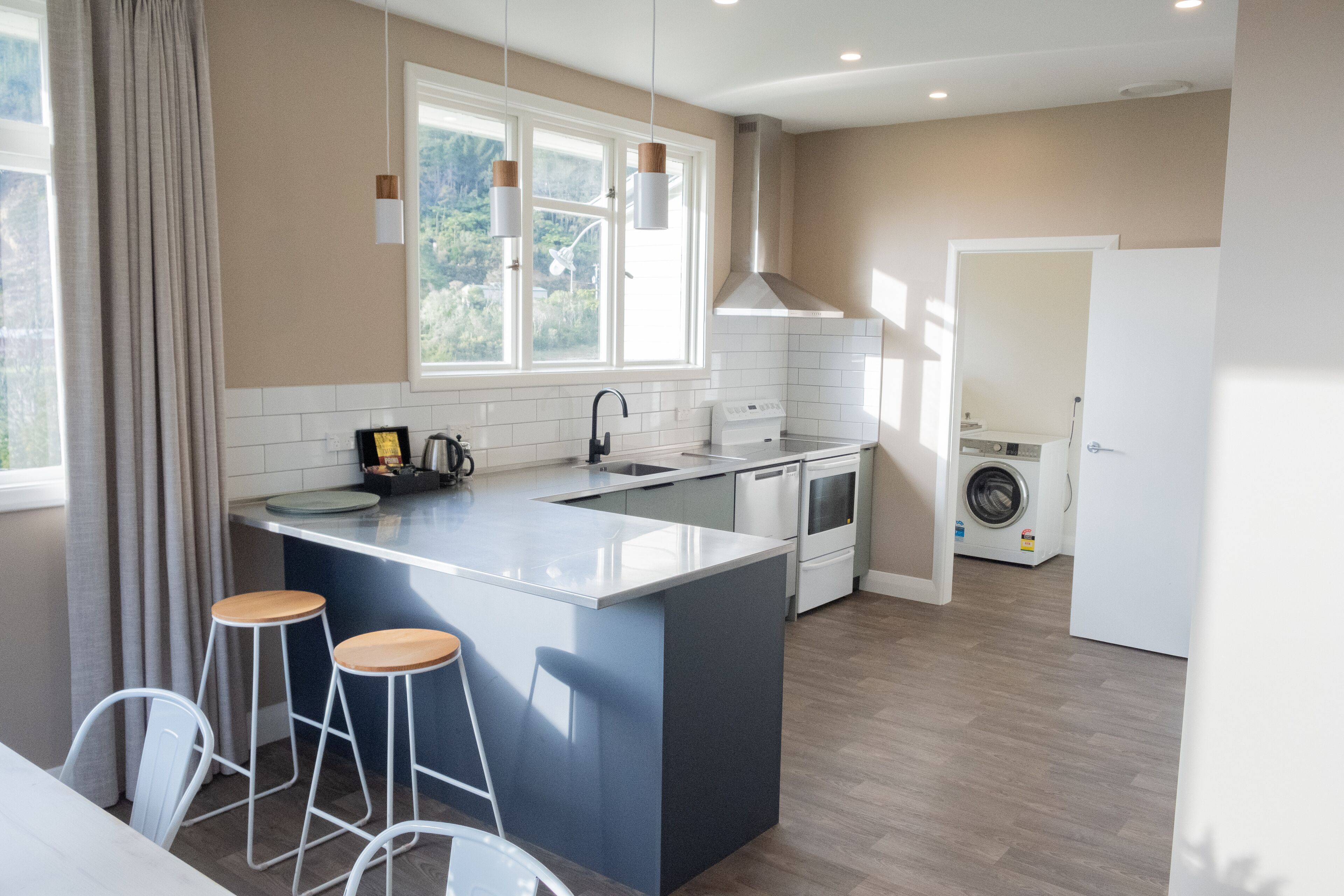 Ett modernt kök med en stor köksö, barstolar, en inbyggd ugn och en tvättmaskin i bakgrunden.