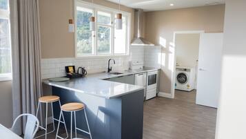 A modern kitchen with a large island, bar stools, a built-in oven, and a washing machine in the background.