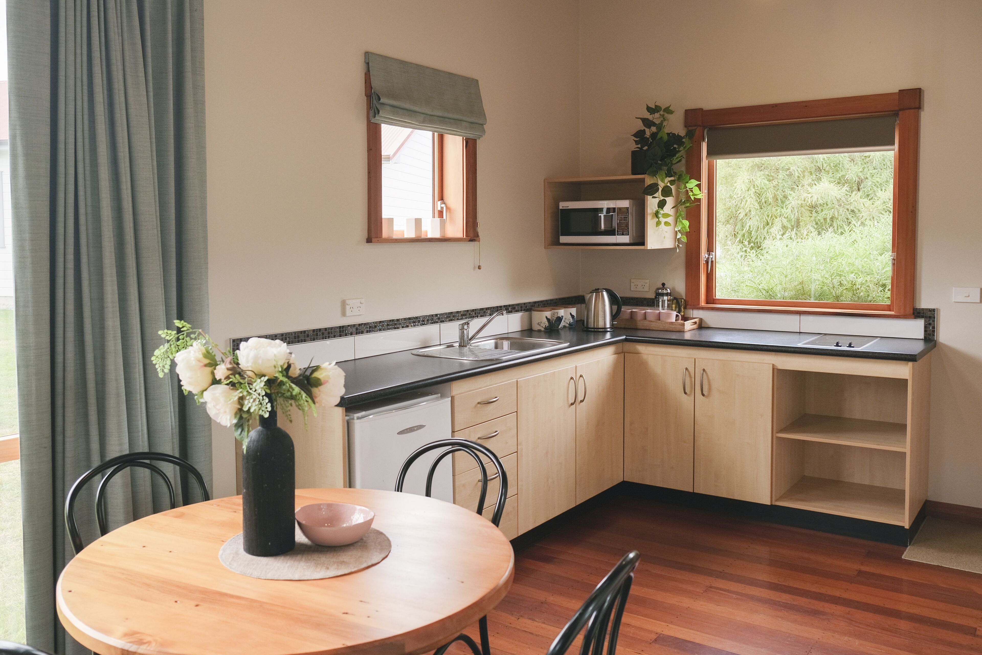 A kitchen with wooden cabinets, a microwave, a sink, and a window with a view of greenery.