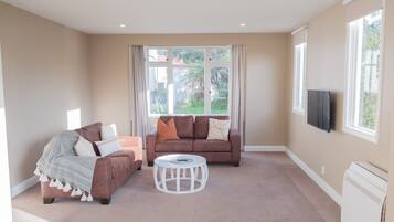 A spacious living room with two sofas, a round coffee table, and a flat-screen TV mounted on the wall.