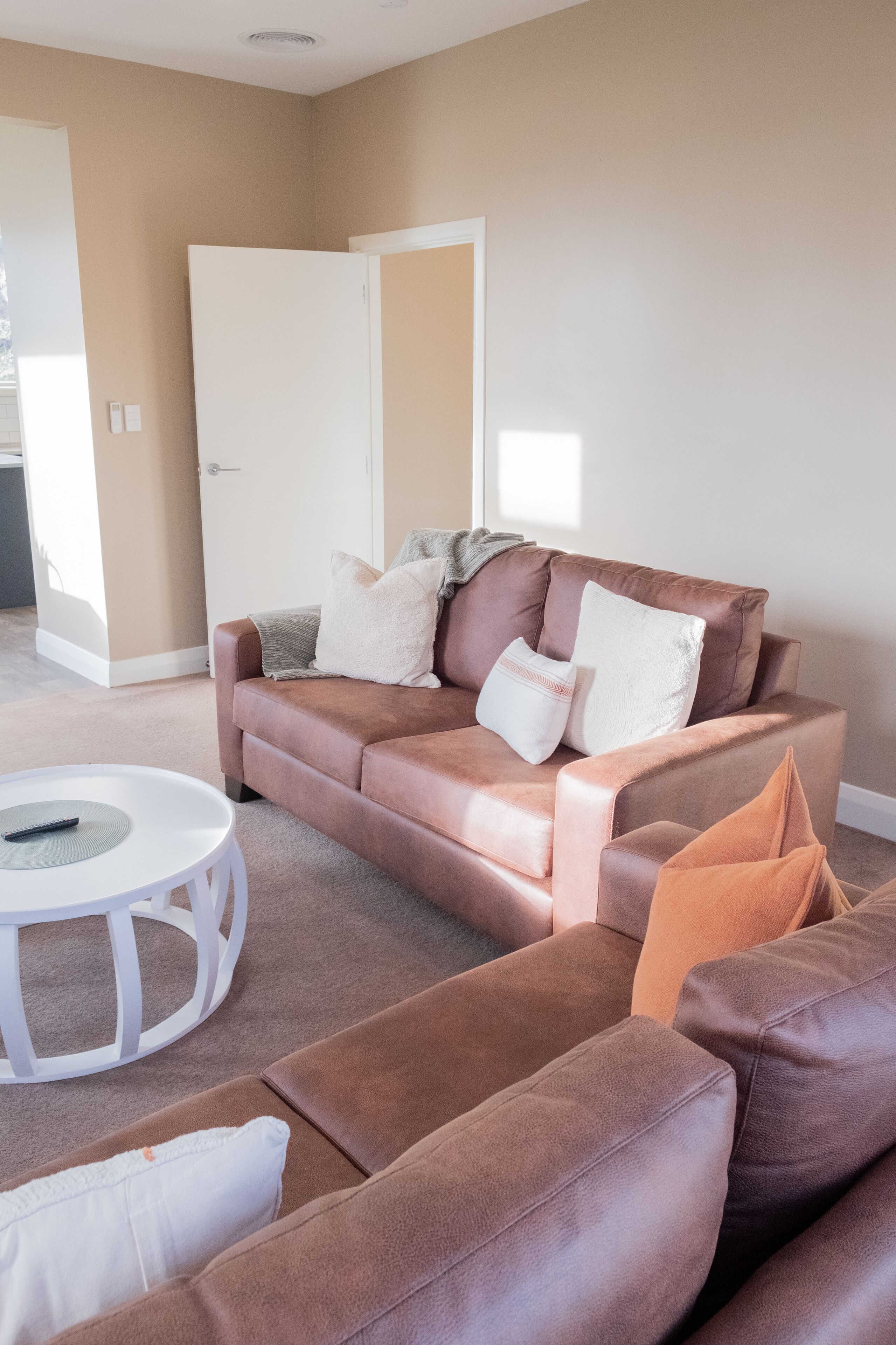 A living room with a brown leather sofa, a white coffee table, and a door in the background.