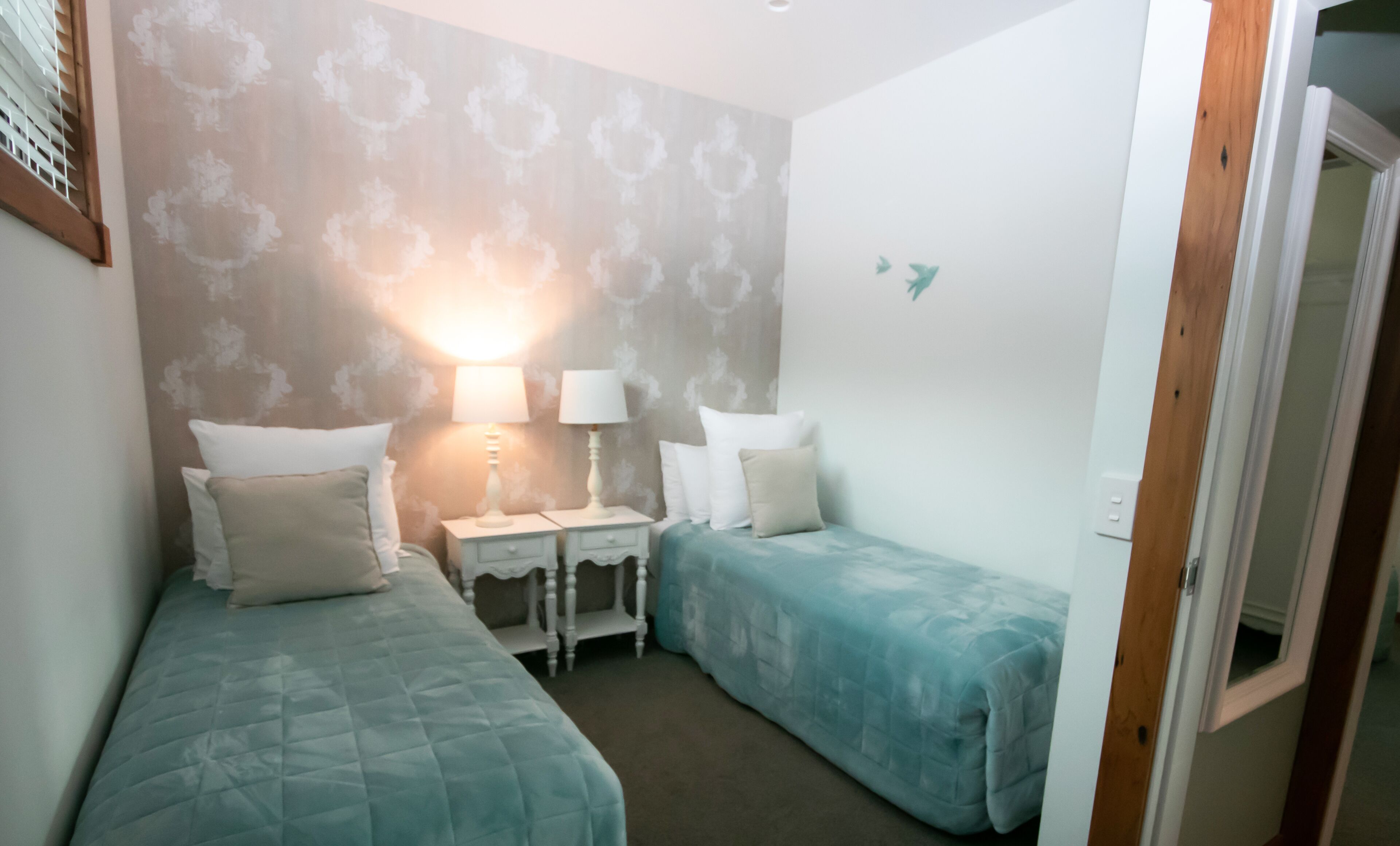 A bedroom with two single beds, a nightstand with a lamp, and a wall with a floral pattern.