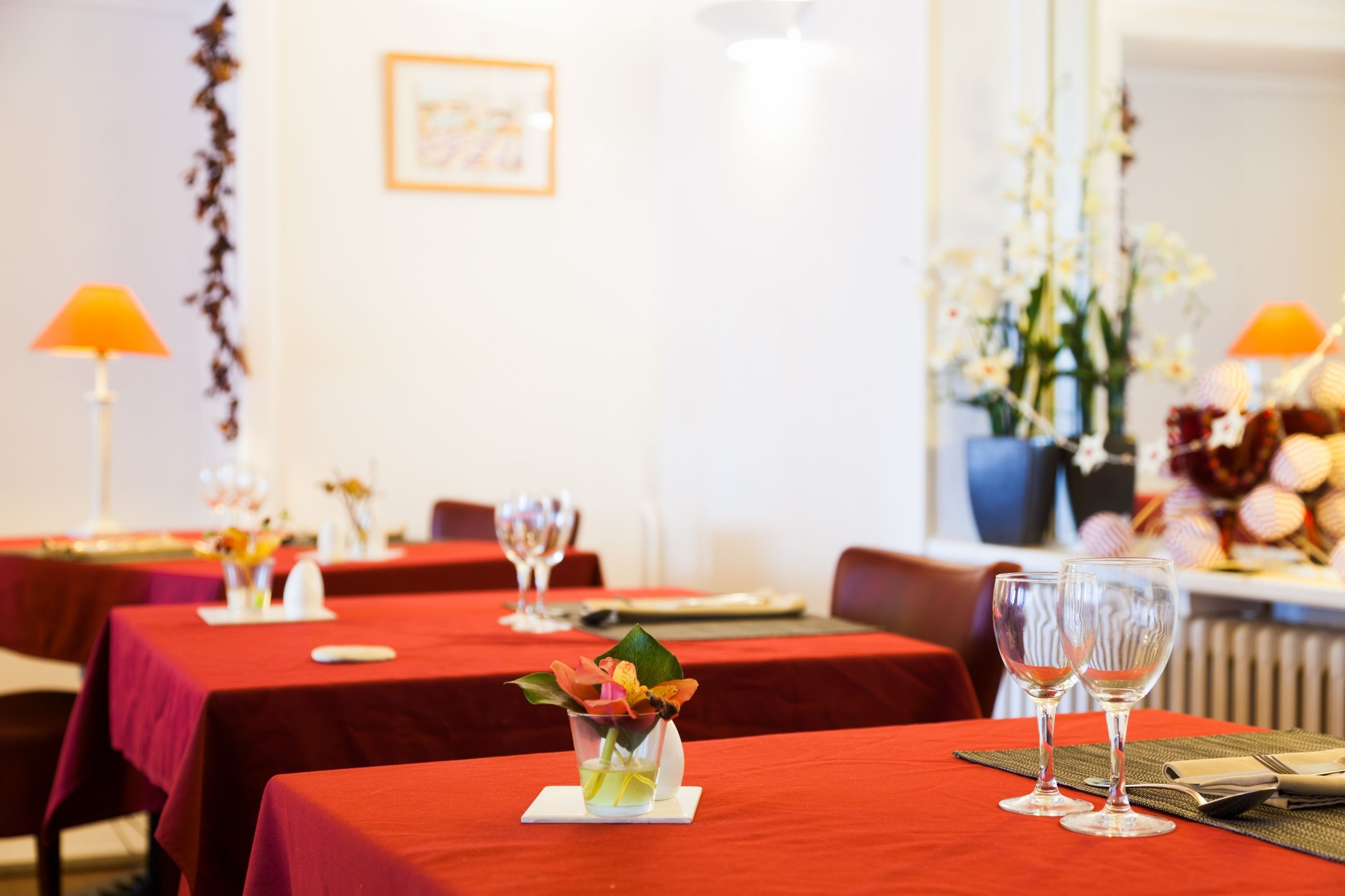 A dining area with tables set for two, each with a small vase of flowers and wine glasses.