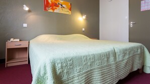 Un dormitorio con una cama, una mesita de noche, una lámpara de pared y una puerta.