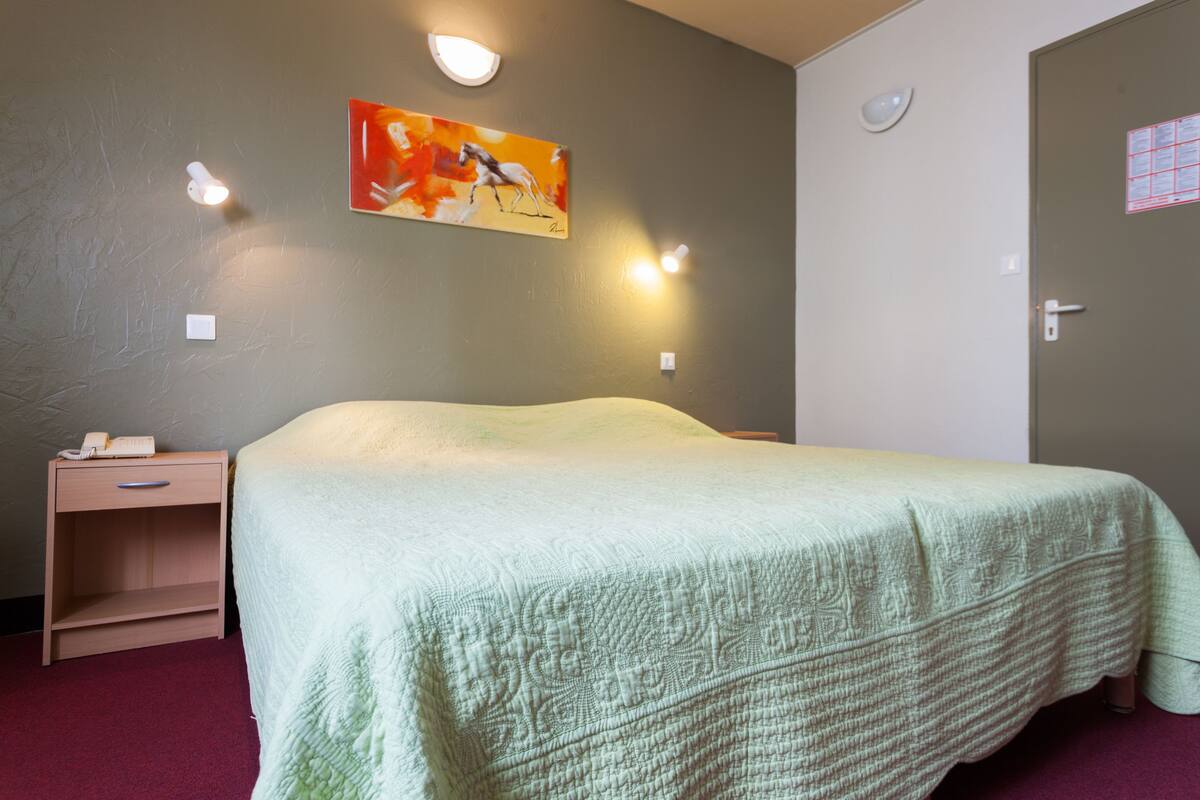 A bedroom with a bed, a nightstand, a wall-mounted light, and a door.