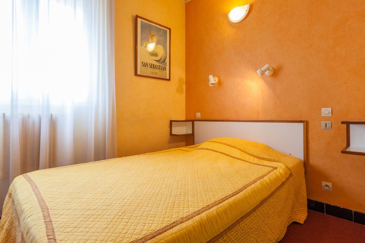 A hotel room with a bed, a framed picture on the wall, and a nightstand with a lamp.