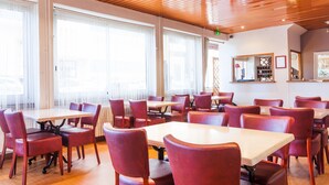 Un restaurante con varias mesas y sillas, ventanas amplias y un techo de madera.