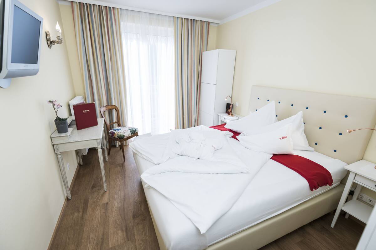 A hotel room with a bed, bedside table, TV, and a desk with a chair.
