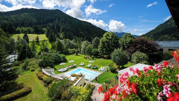 Zona de piscina con sillones de descanso y sombrillas, rodeada de vegetación exuberante y montañas al fondo.