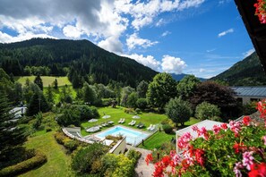 Zona de piscina con sillones de descanso y sombrillas, rodeada de vegetación exuberante y montañas al fondo.