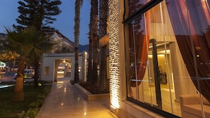 A modern building with a curved glass facade, a well-lit pathway, and palm trees.