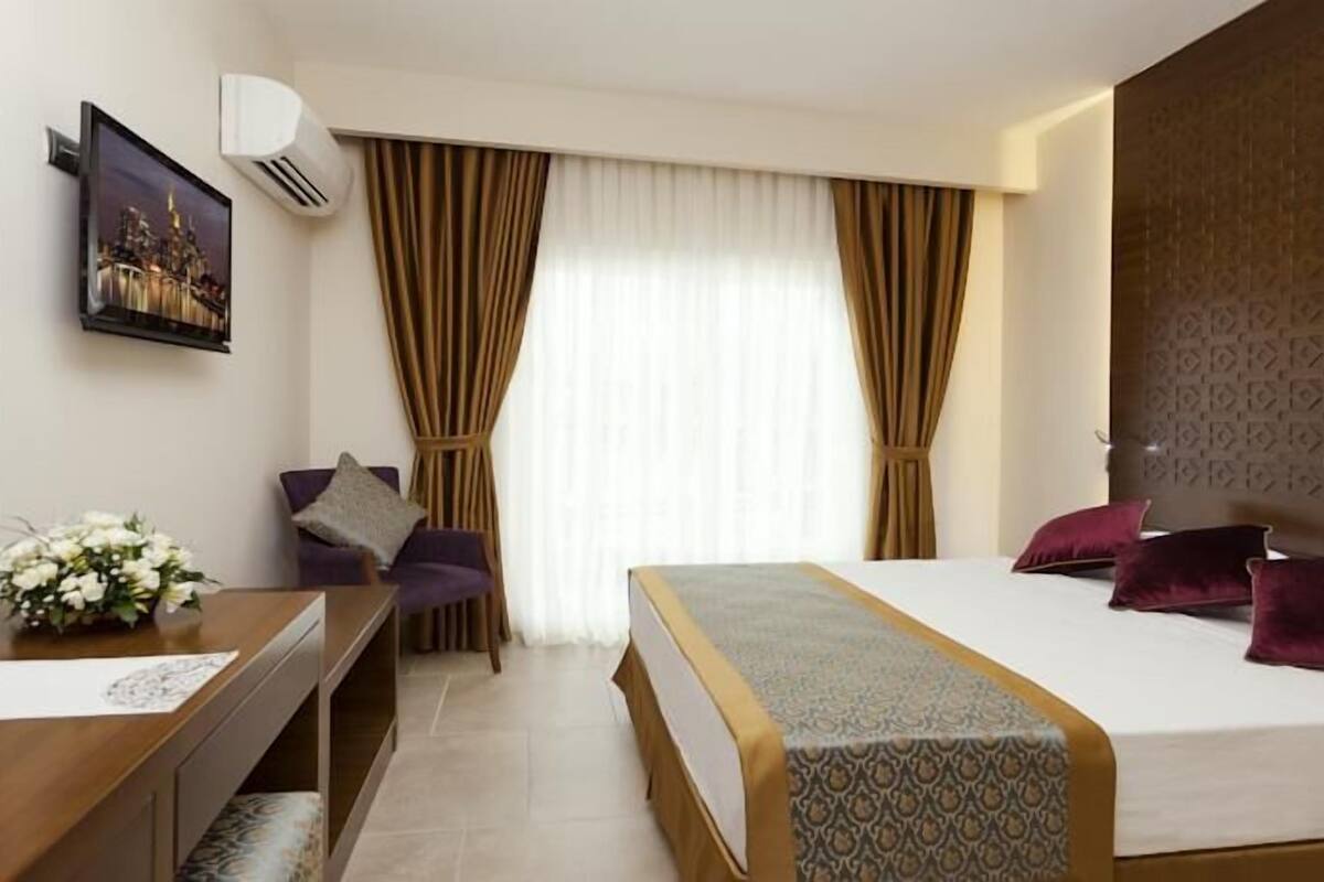 Ein Hotelzimmer mit Bett, Schreibtisch, Stuhl, Fernseher und einem Fenster mit Vorhängen.