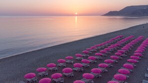 A beach with rows of pink umbrellas and lounge chairs facing the sea at sunset.