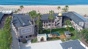 An aerial view of a hotel with a pool, beach umbrellas, and a view of the ocean.