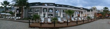Un hotel con zona de piscina, múltiples sillas de descanso y palmeras.