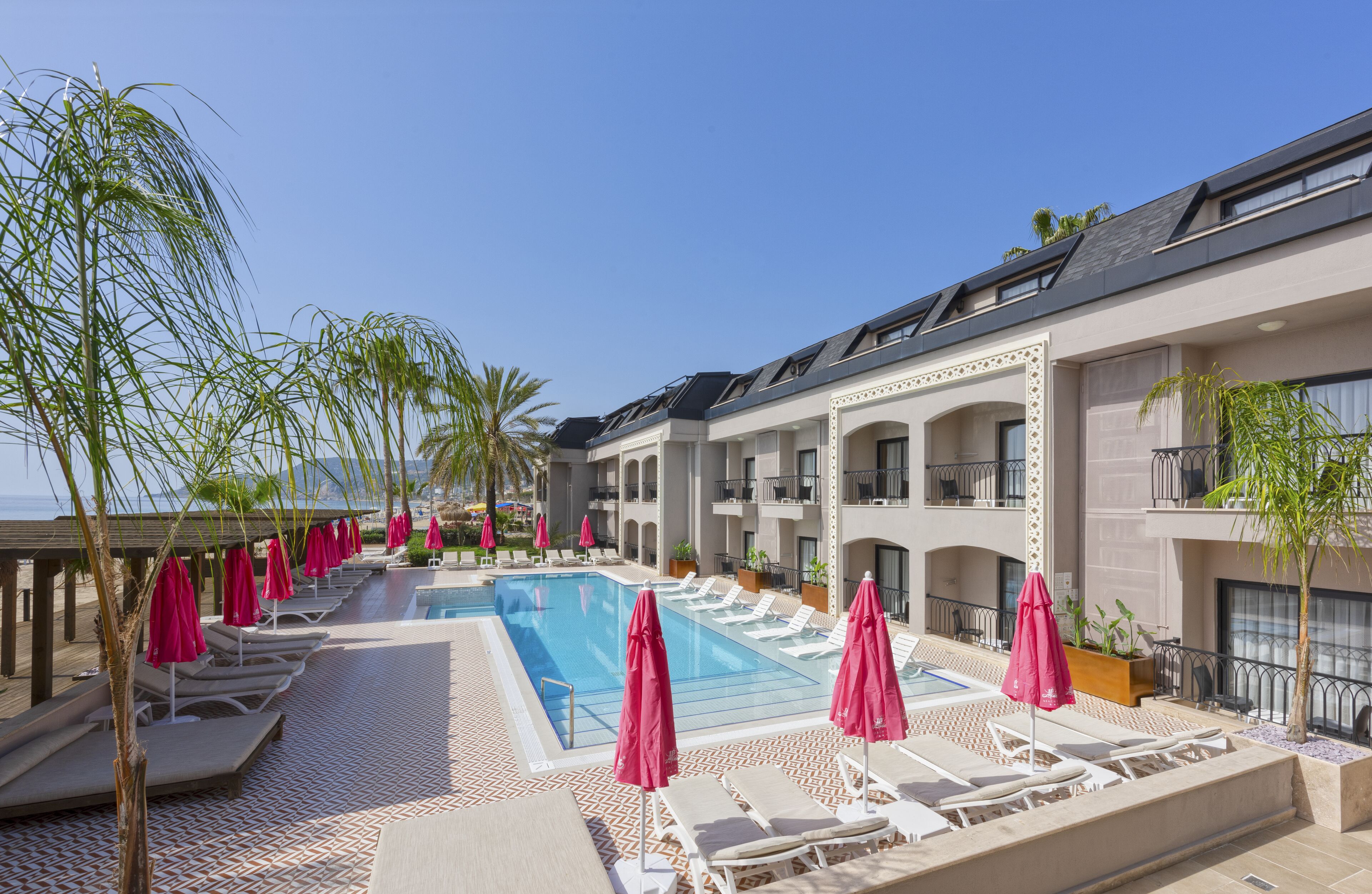 A poolside area with lounge chairs and umbrellas, a swimming pool, and a building with balconies.