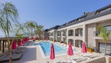 A poolside area with lounge chairs and umbrellas, a swimming pool, and a building with balconies.