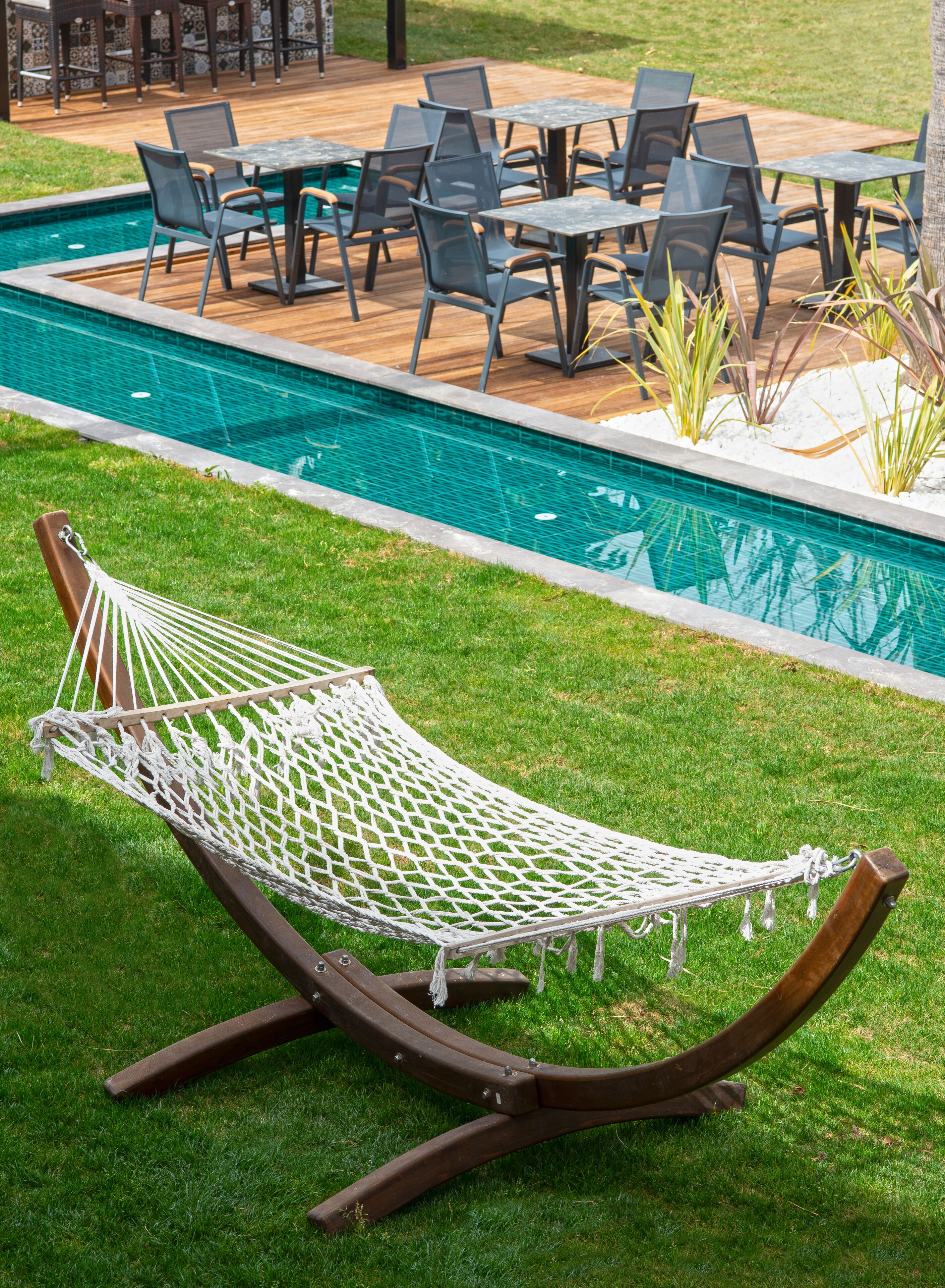 Eine Hängematte auf einer Rasenfläche neben einem Schwimmbecken mit Gartenmöbeln und Tischen.