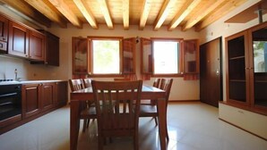 Une cuisine spacieuse dotée de meubles en bois, d’une table à manger avec des chaises et de grandes fenêtres laissant entrer la lumière naturelle.