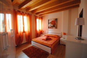 Une chambre avec un plafond en bois, un lit avec une literie orange, une table de chevet, une lampe et un tableau au mur.