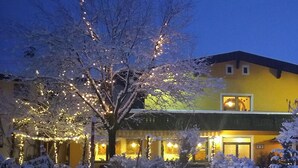 Un hotel con fachada amarilla, ventanas iluminadas y árboles cubiertos de nieve.