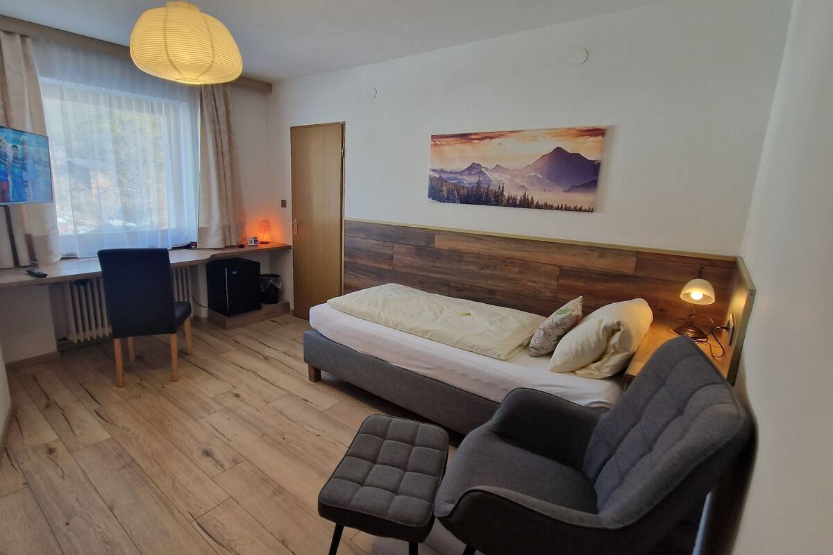 Habitación de hotel con cama, escritorio con computadora, silla, televisor y un cuadro en la pared.