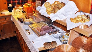 Un bufé con diversos alimentos, como pan, pasteles y platos de carne, dispuesto sobre una mesa con mantel blanco.