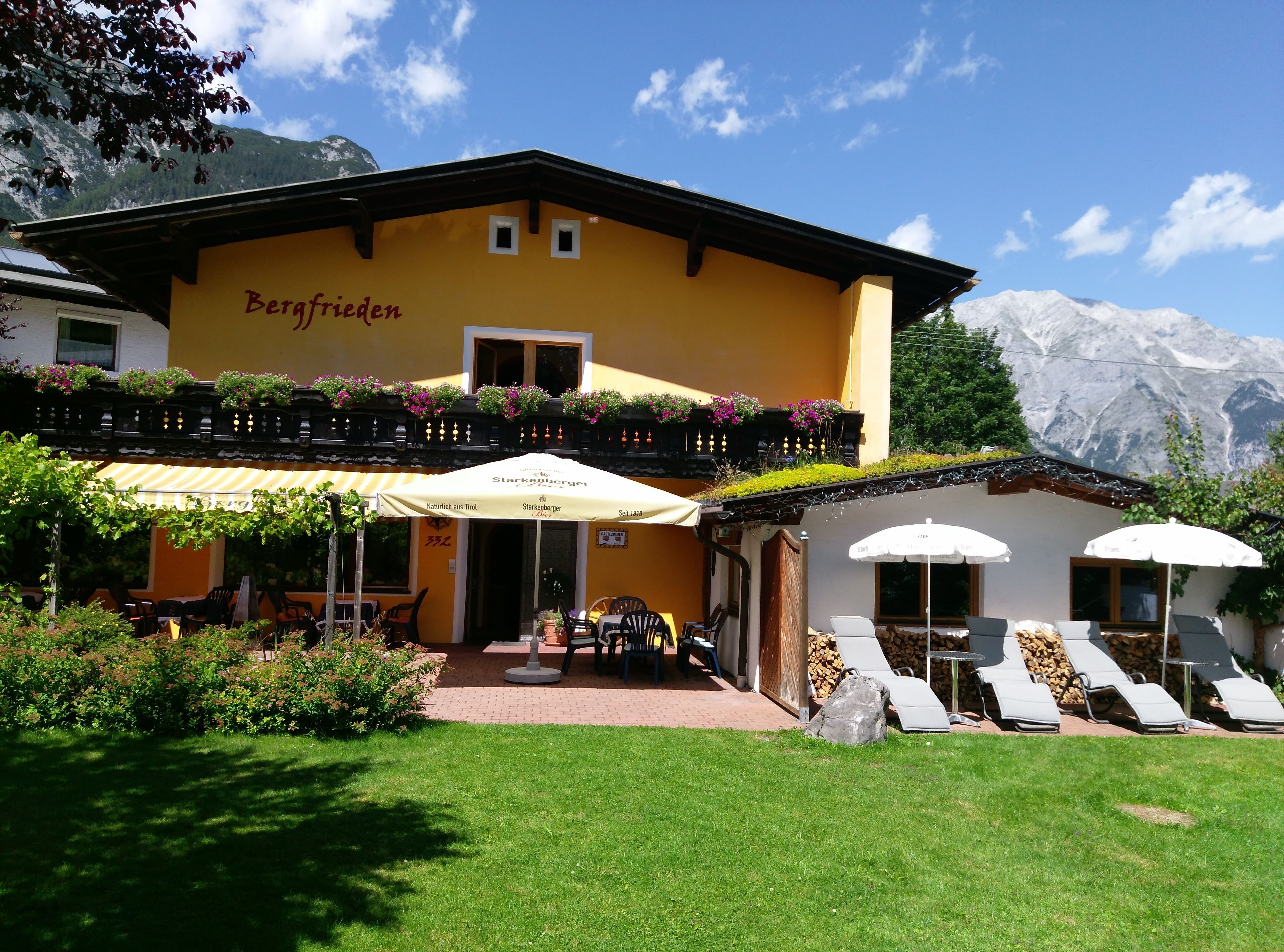 A yellow building with a sign reading "Bergfrieden" and outdoor seating with umbrellas.