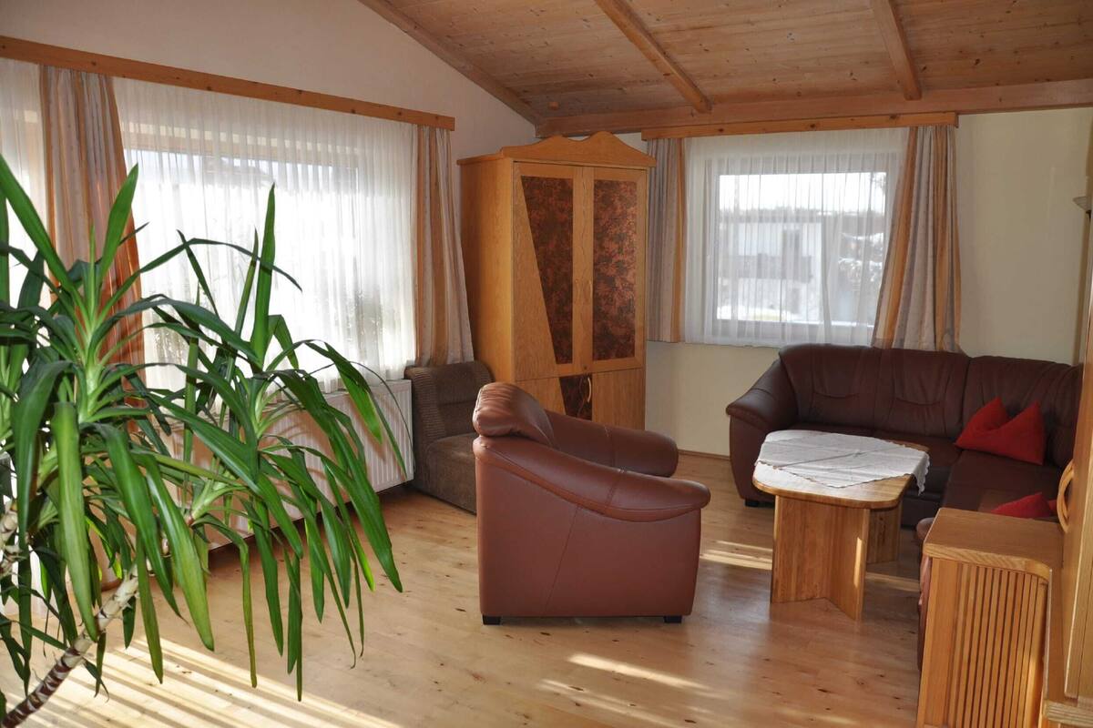 Una sala de estar con un sofá de cuero marrón, un sillón marrón, una mesa de centro de madera y una planta grande en maceta.