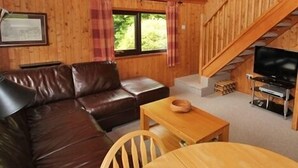 Ein Interieur einer Holzhütte mit einem braunen Ledersofa, einem Holztisch, einem Fernseher und einer Treppe.