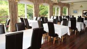 Ein Restaurant mit mehreren Tischen und Stühlen, großen Fenstern mit Vorhängen und hängenden Pendelleuchten.