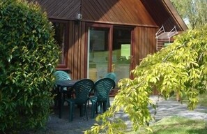 Eine Holzhütte mit einer überdachten Terrasse, grünen Stühlen und einem kleinen Tisch.