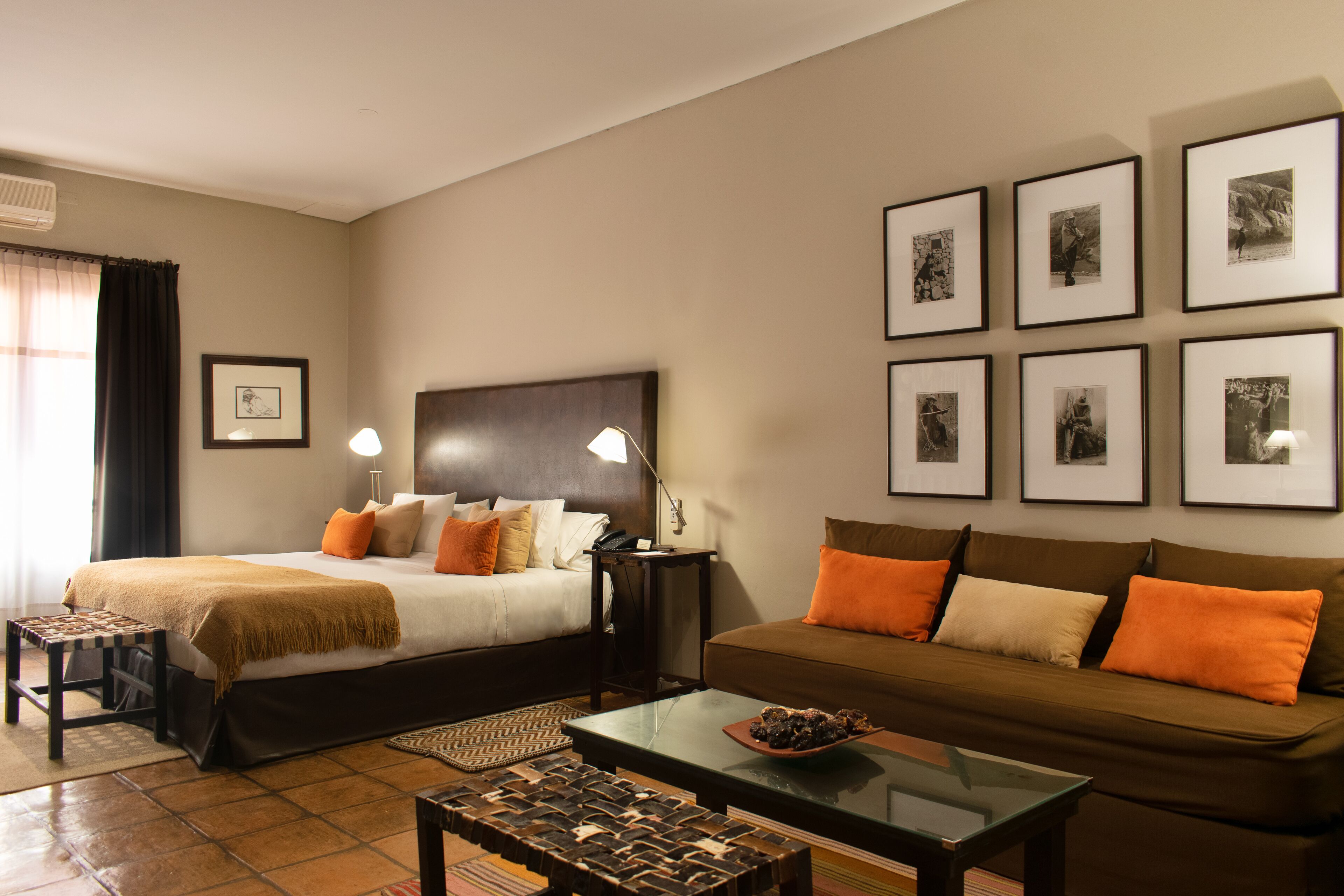 A hotel room with a bed, a sofa, a coffee table, and framed pictures on the wall.